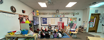 A group of children sitting on the floor listening to teachers