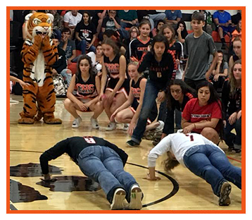 Students cheering on two students in a fun push-ups competition during a basketball game